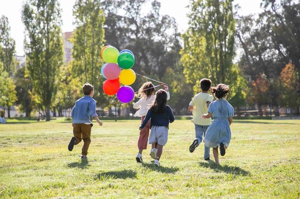 Bambini che corrono in un parco con palloncini colorati, simbolo di divertimento e natura.