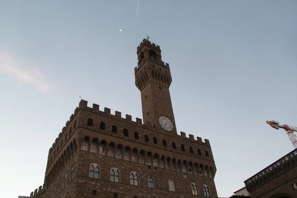Vista del Palazzo Vecchio a Firenze con il cielo al tramonto, torre e orologio ben visibili.