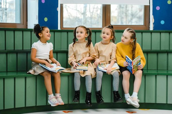Bambini seduti su una panca verde leggendo libri in una biblioteca per bambini.
