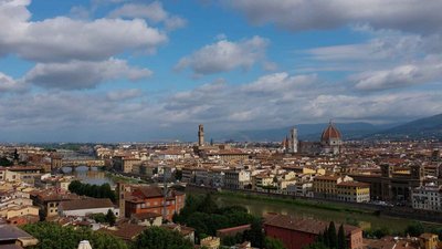 Panoramic view of Florence with the Duomo, Ponte Vecchio, and the Arno River under a partly cloudy sky.