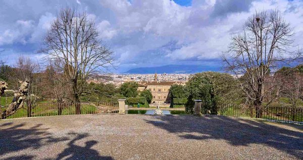 View of the Boboli Gardens in Florence with trees, a fountain, and the city in the background under a cloudy sky.