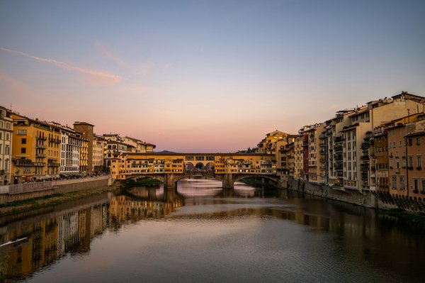 A rowboat on the Arno River at sunset with Ponte Vecchio glowing gold in the background.