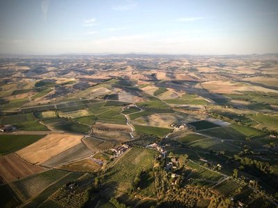 Panoramic view of Tuscany with rolling hills, vineyards, and farmhouses at sunset.