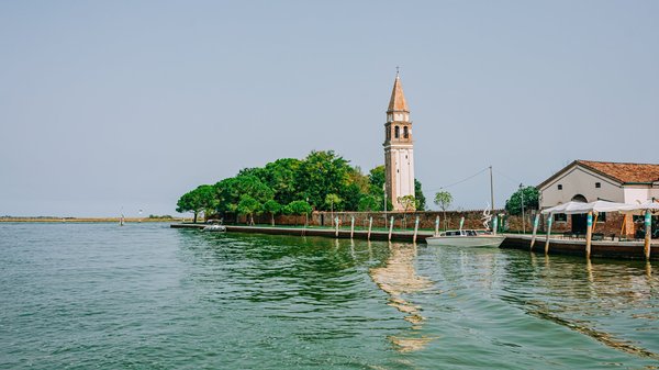 Open water of the Venetian lagoon with a bell tower rising above a distant island.