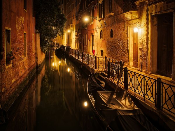 A dimly lit Venetian canal-side alley at night, with a moored gondola and lantern light.