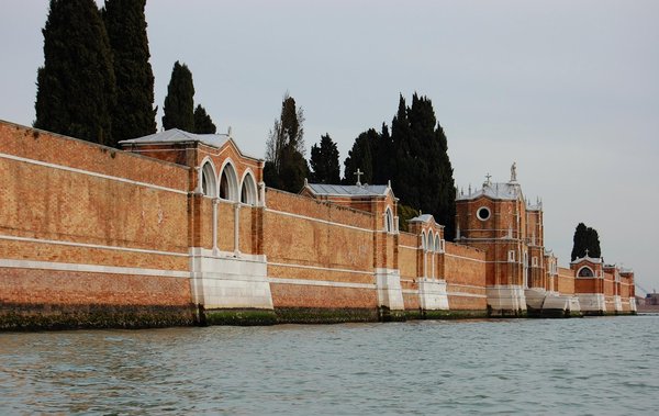 The crenellated brick perimeter wall of San Michele cemetery island in the Venetian lagoon, lined with cypress trees.