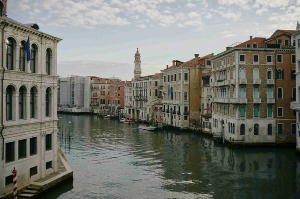 View of a Venetian canal with historic buildings and a tower in the background, near the Museum of Palazzo Mocenigo.