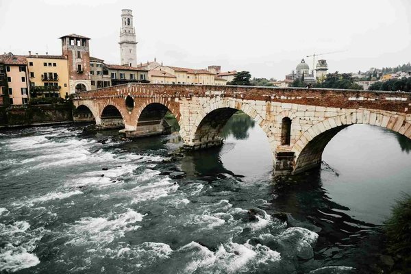 Ponte Pietra in Verona with the Adige River and historic architecture in the background on a cloudy day.