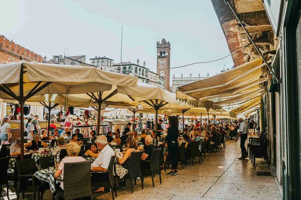 Romantic outdoor dinner in Piazza delle Erbe in Verona, with tables under umbrellas and a view of historic architecture.