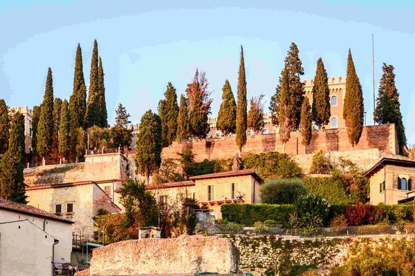 Sunset view of Castel San Pietro in Verona with cypress trees and historic walls.