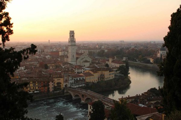 Evening view of the Adige River and Ponte Pietra in Verona with the bell tower and city in the background.