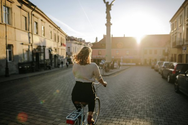 Donna in bicicletta vicino alla statua dell'Angelo di Užupis al tramonto, Vilnius, Repubblica di Užupis.