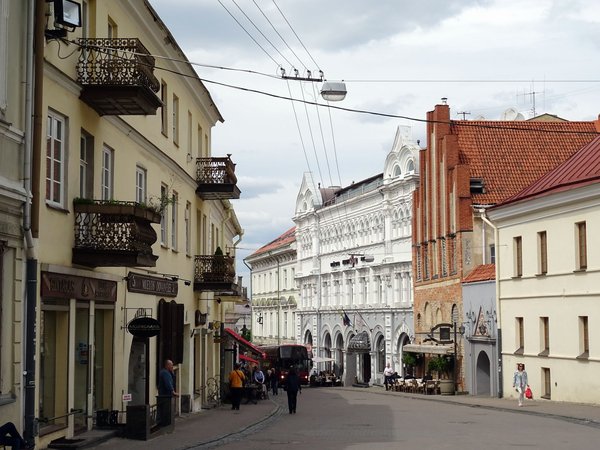 Strada Pilies a Vilnius con edifici storici, balconi decorati e persone che passeggiano.