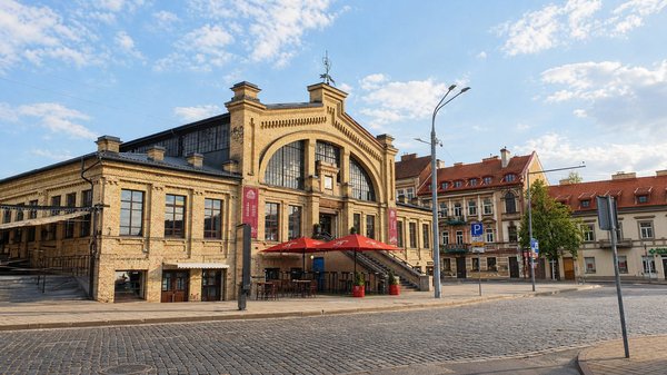 Facciata del Mercato Hales a Vilnius con cielo sereno e ombrelloni rossi all'esterno.