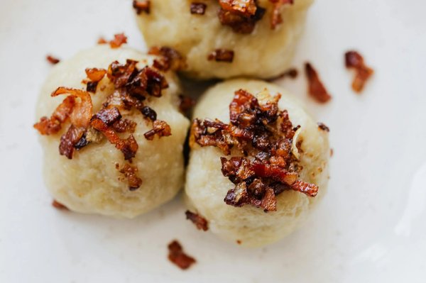 Close-up of Lithuanian cepelinai with crispy bacon, a traditional dish at Kalvarijų Market in Vilnius.