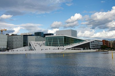 View of the Oslo Opera House with a blue sky and water in the foreground.
