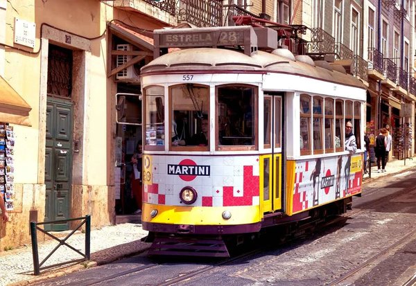 Tram 28 in Lisbon with colorful decorations, passing through a historic street with traditional buildings.