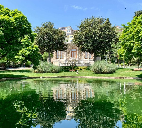Gulbenkian Garden in Lisbon with reflective pond, green trees, and historic building in the background.
