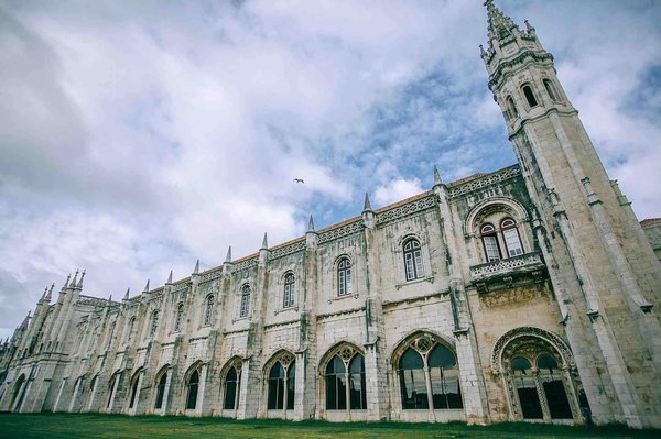 Facade of the Jerónimos Monastery in Lisbon with a cloudy sky in the background.