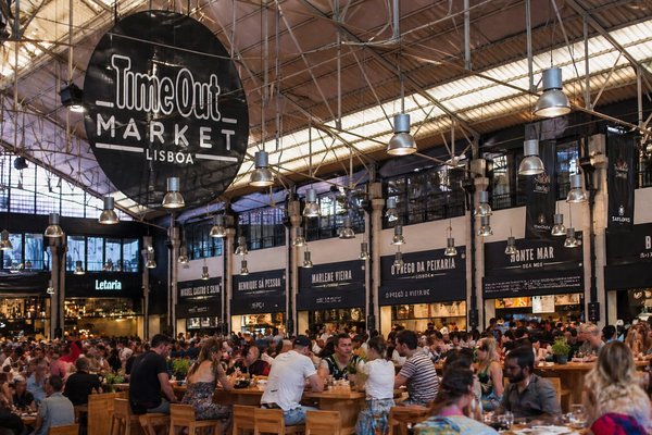Interior of Time Out Market Lisbon with people dining and the market logo prominently displayed above.