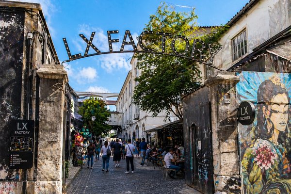 Entrance to LX Factory in Lisbon with iconic sign, colorful murals, and people walking and relaxing.