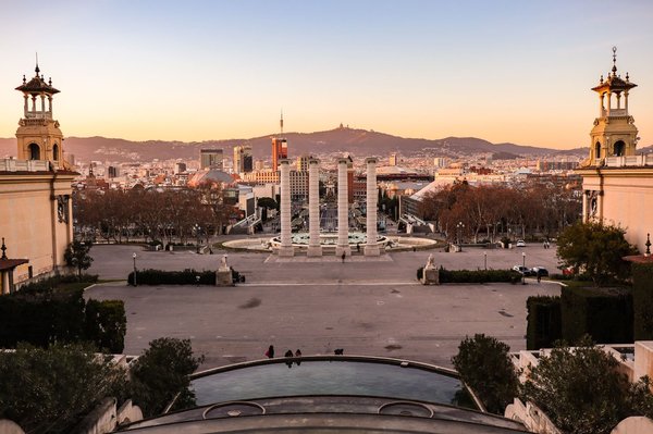 Sunset view from Montjuic's terrace over the Magic Fountain and Barcelona's skyline, with people relaxing on the ledge.