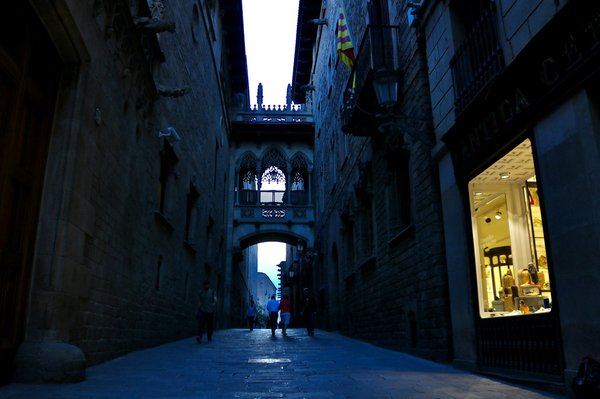The Gothic Quarter's iconic neo-Gothic bridge over Carrer del Bisbe at blue hour, with people strolling below.