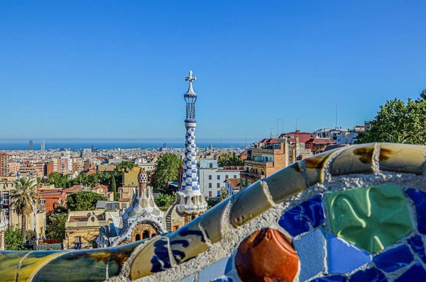 View of Barcelona from Park Güell with colorful mosaics and iconic architecture under a blue sky.