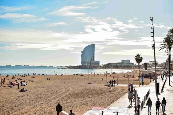 Barceloneta Beach in Barcelona with the iconic W Hotel and people walking and relaxing.
