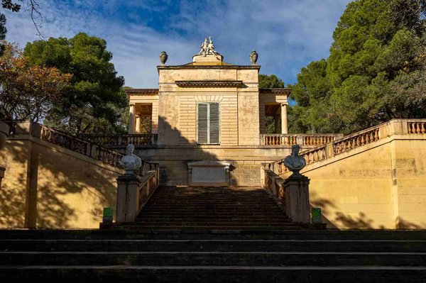 Staircase and historic building in Parc del Laberint d'Horta in Barcelona, surrounded by trees and blue sky.