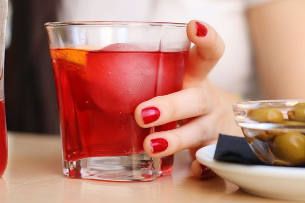 A glass of red vermouth on ice with an orange slice, served with a bowl of olives on the side.
