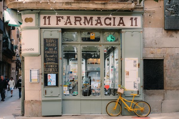 A charming historic Barcelona storefront with Catalan signage, string lights, and a yellow bicycle parked outside.