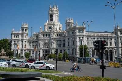 Palacio de Cibeles in Madrid with traffic and cyclist in foreground, clear blue sky.