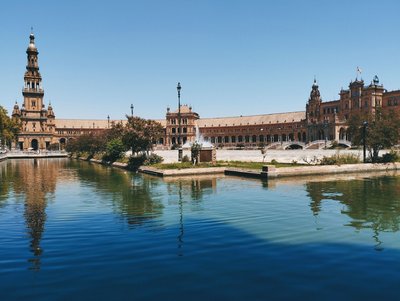 Panoramic view of Plaza de España in Seville with historic architecture and water canal under a clear blue sky.