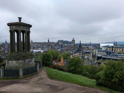 View of Dugald Stewart Monument on Calton Hill with Edinburgh skyline in the background on a cloudy day.