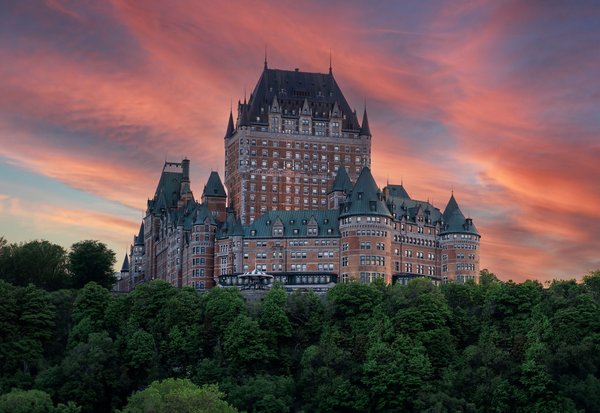View of Château Frontenac in Quebec City at sunset, with colorful sky and greenery in the foreground.