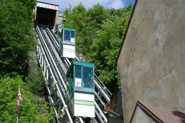 Quebec City funicular connecting upper and lower town, surrounded by greenery and blue sky.
