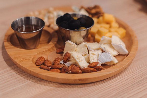 Tasting platter with cheese, almonds, olives, and honey on a wooden table.