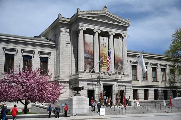 Facade of the Museum of Fine Arts in Boston with blooming cherry tree and visitors.