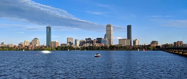 View of the Charles River with boats and Boston's skyline on a sunny day.