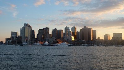 Boston skyline at sunset with skyscrapers and boats in the harbor.