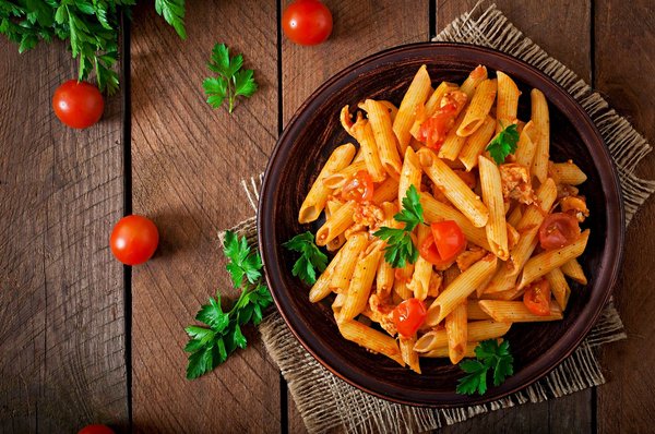 Plate of penne pasta with tomato sauce, cherry tomatoes, and parsley on a wooden table.