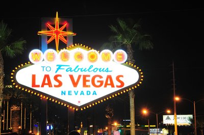 Iconic 'Welcome to Fabulous Las Vegas' sign lit up at night with palm trees and city lights in the background.