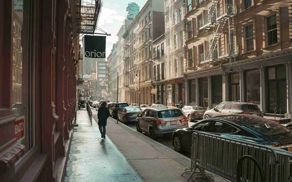 Strada nel quartiere Soho di New York con edifici in ghisa, auto parcheggiate e pedoni.