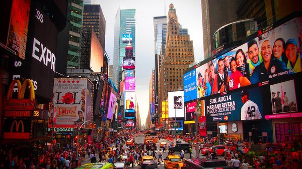 Times Square a New York con cartelloni pubblicitari luminosi, taxi gialli e una folla di persone.