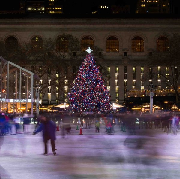 Pattinatori sul ghiaccio a Bryant Park con un grande albero di Natale illuminato, New York durante il periodo natalizio.