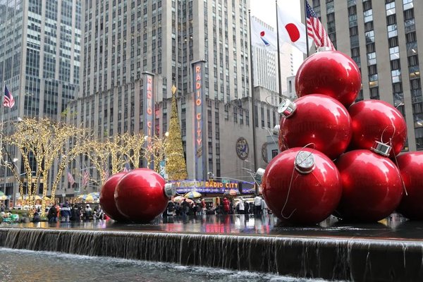 Decorazioni natalizie a New York con grandi ornamenti rossi, luci scintillanti e Radio City Music Hall sullo sfondo.