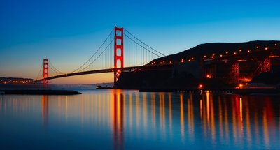 Night view of the illuminated Golden Gate Bridge with reflections on the water in San Francisco.