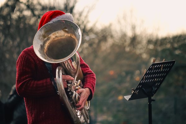 Musicista di strada con cappello da Babbo Natale che suona uno strumento a fiato all'aperto leggendo lo spartito, in un concerto natalizio open-air.