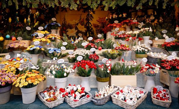 Bancarella di un mercatino di Natale ricca di decorazioni artigianali, statuine in ceramica e bouquet di fiori esposti sotto ghirlande di pino.